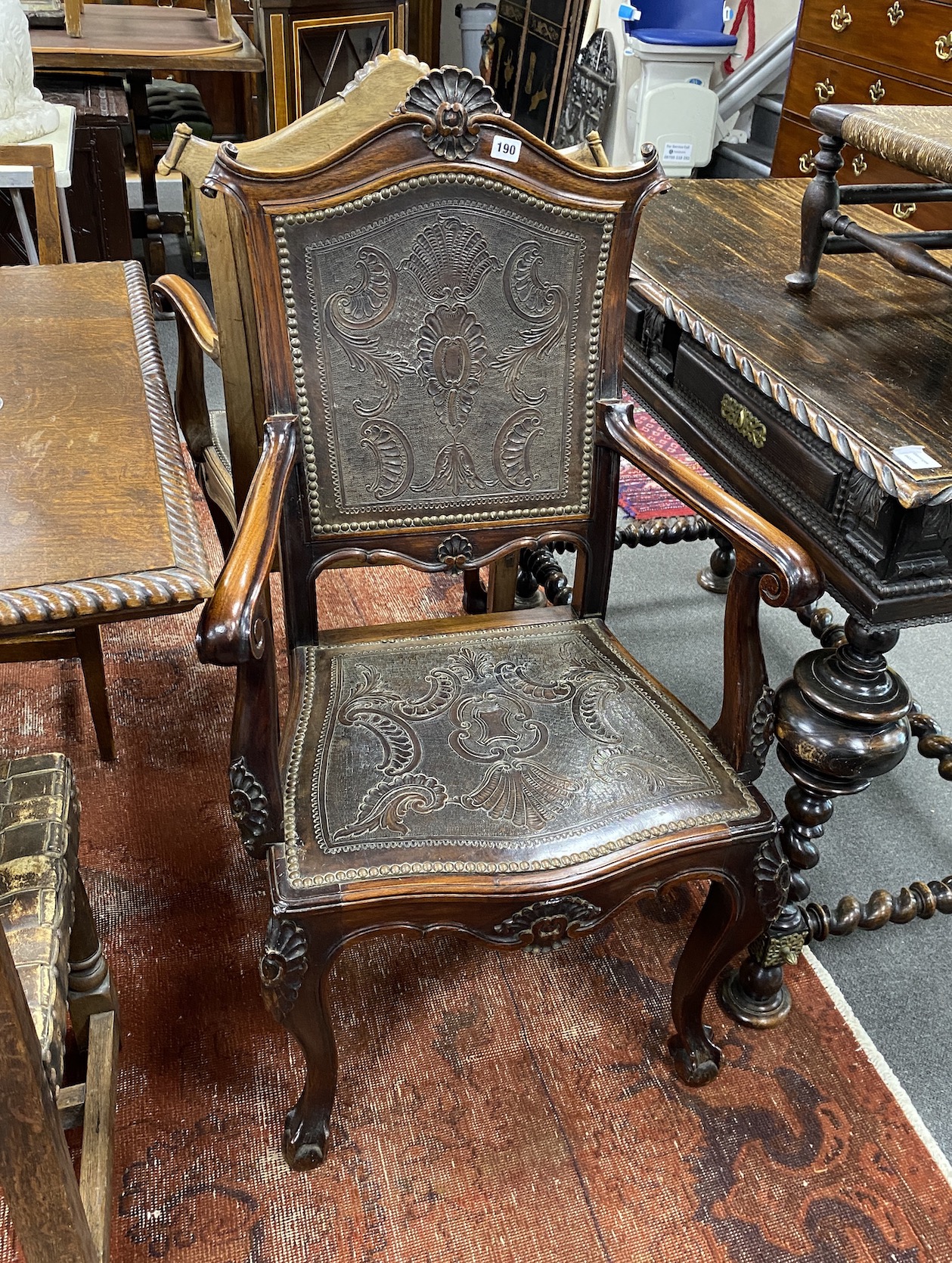 A pair of continental Spanish style carved elbow chairs with tooled leather backs and seats, width 62cms height 108cms.